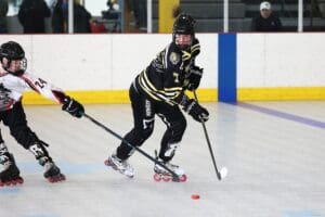 Inline hockey players competing on a rink, one in black jersey controlling the puck while evading an opponent.