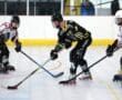 Three roller hockey players competing on an indoor rink, wearing protective gear and uniforms.