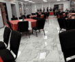 Spacious event room with red and white tablecloths, marble floors, and framed pictures on the walls.