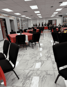 Spacious event room with red and white tablecloths, marble floors, and framed pictures on the walls.