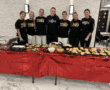 Women's team in Tigers shirts standing behind a buffet table with salad and bread.