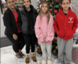 Family posing by a decorated Christmas tree indoors, with festive ornaments and smiling faces.