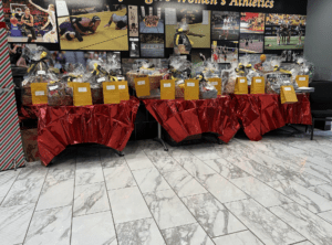 Sports event raffle prizes on tables with red covers, featuring yellow gift bags and wrapped baskets.