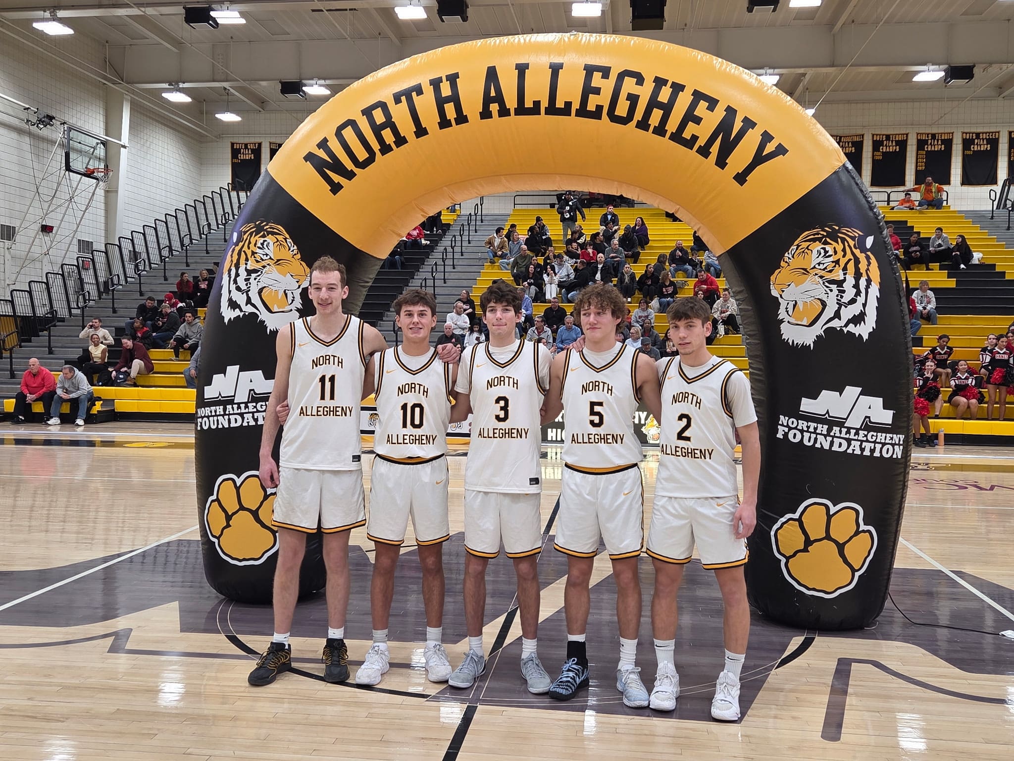 Five North Allegheny basketball players pose under an arch in the gym.
