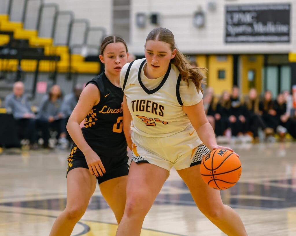 High school girls' basketball game, player dribbling past defender on the court.