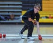 Person playing bocce ball indoors, preparing to roll a red ball with focus, sports background.