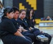 A group of young athletes sitting on chairs in a gymnasium, wearing team uniforms.