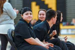 Young athletes sitting on a bench at a sports event, wearing matching black uniforms, with focus on camaraderie.