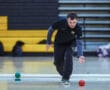 Person playing bocce indoors, focused and poised for a throw on a gym floor.