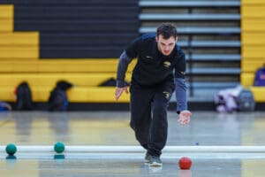 Person playing bocce indoors, focused and poised for a throw on a gym floor.