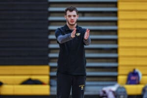 Young coach instructs with hand gestures on indoor court, wearing black sportswear.