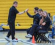 Team members in a gymnasium high-five while others watch, seated near a scoreboard, showing teamwork and engagement.