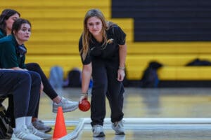 Woman playing bocce ball indoors, aiming with focus amidst a supportive audience.