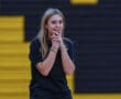 Young woman in black shirt with bracelets, standing in gym, hands clasped, expressing excitement or anticipation.