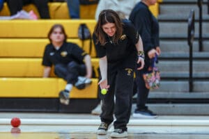 Young athlete playing bocce indoors, focusing on precision, wearing team uniform.