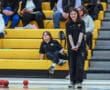 Person enjoying a bocce game in a gymnasium with a seated audience on yellow bleachers.