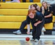 Athlete rolling a red ball in a gym, focused with spectators in the background on yellow bleachers.