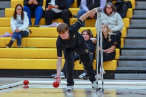 Athlete with crutches plays boccia in a gym, showcasing determination and adaptive sports skills.
