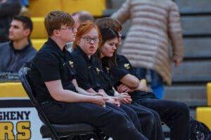 A group of young people in black uniforms sitting on a bench at an indoor sports event.