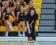 A person bowling with intense focus, surrounded by a cheering squad in a gymnasium.