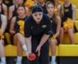 Focused bocce player about to throw, surrounded by cheerleaders with yellow pom-poms in a sports arena.
