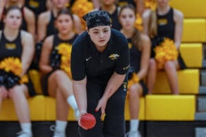 Focused bocce player about to throw, surrounded by cheerleaders with yellow pom-poms in a sports arena.