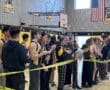 School athletes and students in a gym cheer for teammates during a sports event, with caution tape marking boundaries.