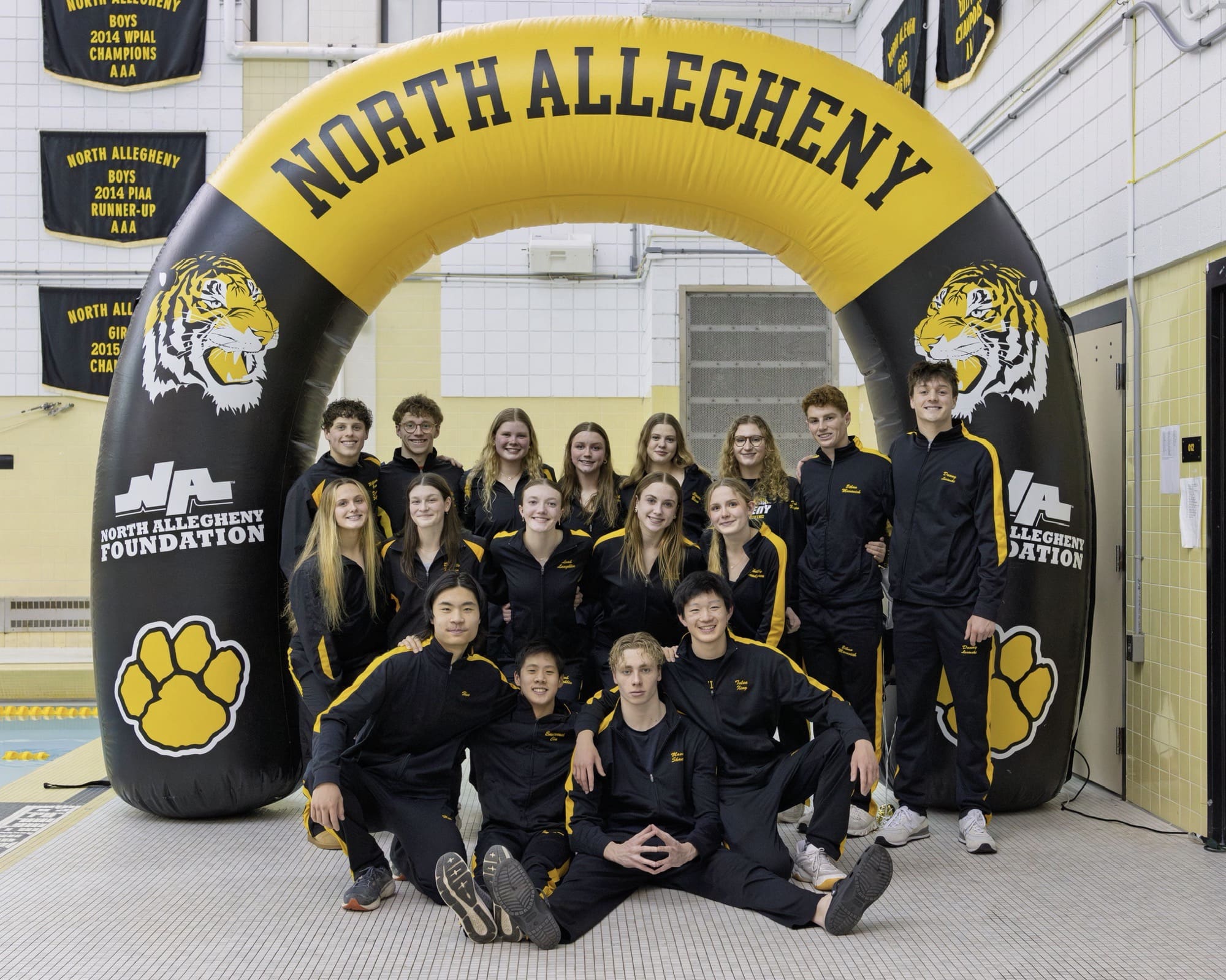 North Allegheny swim team group photo under school banner at indoor pool with championship banners in background.