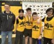 Youth rowing team poses with coach in yellow uniforms at a sports event backdrop.