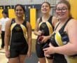 Three student athletes in black and yellow sports attire smiling in a gym setting.