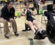 Person rowing on a machine with a coach beside them, focused on fitness training indoors.
