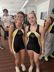 Two athletes in matching NA Crew uniforms smiling indoors at an event.
