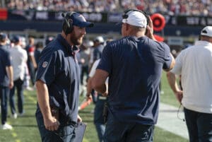 Coaches strategize on the sideline during a football game, wearing team gear and headsets.