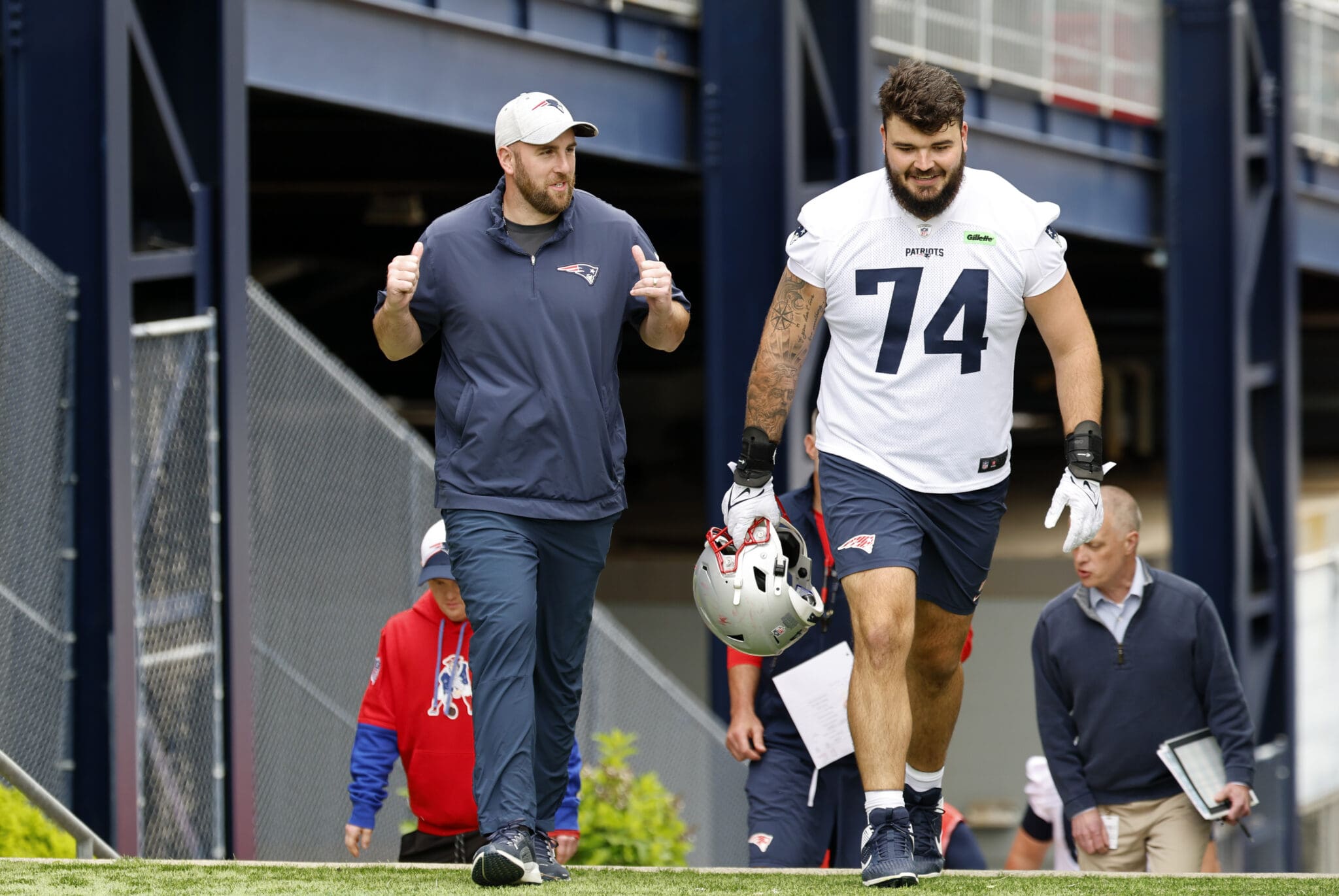 Football player and coach at Patriots training session, walking and smiling.