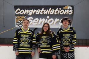 Three senior ice hockey players in North Allegheny jerseys celebrate in front of a Congratulations Seniors banner.