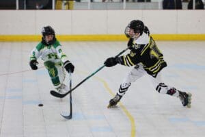 Two junior hockey players in action at an indoor roller hockey game, focusing on the puck.