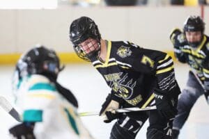 Youth ice hockey game, player in black jersey with number 7 skates towards opponent on rink.