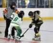 Two inline hockey players face off as the referee prepares for the puck drop on the rink, wearing safety gear.