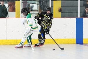 Two players on rollerblades compete for the puck in an intense inline hockey match on the rink.