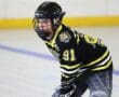 Hockey player in black and yellow jersey focuses during a game on ice rink, wearing a helmet and holding a stick.