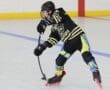 Hockey player in black and yellow uniform skating and handling puck on indoor rink.