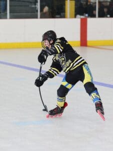 Hockey player in black and yellow uniform skating and handling puck on indoor rink.