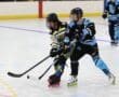 Two players compete for the puck in a roller hockey match on an indoor rink.