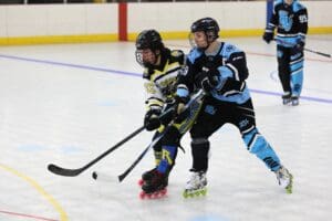 Two players compete for the puck in a roller hockey match on an indoor rink.
