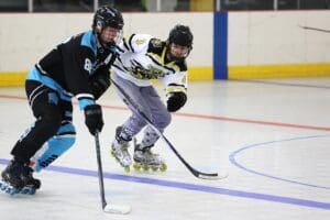 Two roller hockey players competing on the rink in intense action, wearing black and white uniforms.