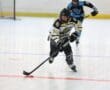 Youth roller hockey player in action, wearing a white and yellow jersey, focused on the puck during a game.