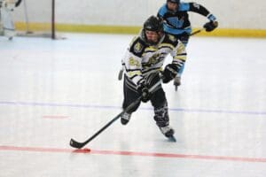 Youth roller hockey player in action, wearing a white and yellow jersey, focused on the puck during a game.