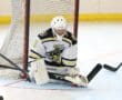 Hockey goalie making a save on the ice, kneeling with protective gear and a stick, during an intense game.