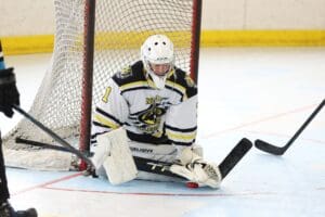 Hockey goalie making a save on the ice, kneeling with protective gear and a stick, during an intense game.