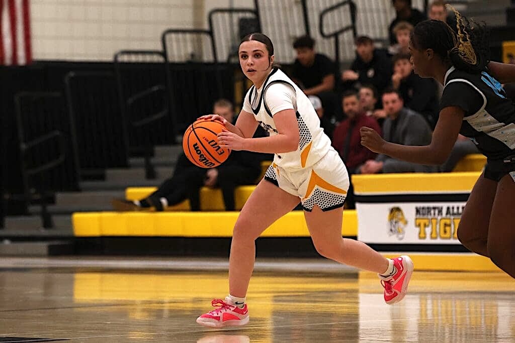 Basketball player in white uniform dribbles past defender during a game in a gym.